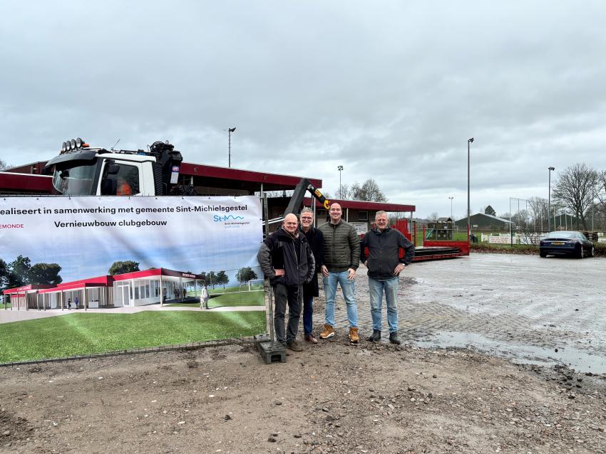 4 mannen staan langs een doek met een afbeelding van het vernieuwde clubgebouw. Achter hen rijdt een vrachtwagen en het clubgebouw en de velden zijn ook te zien.